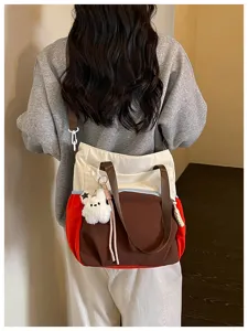 Vue de dos d’un sac cabas bicolore porté en bandoulière, avec anses brunes et ourson en peluche