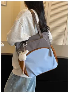 Sac en nylon gris, bleu et brun porté à l'épaule, avec des sangles brunes et un lapin en peluche