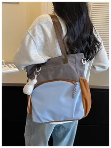Vue de dos du sac bicolore avec poche zippée et pompon blanc en peluche, porté à l’épaule