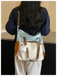 Vue arrière d’une femme portant un cabas bicolore, avec bandoulière brune et charm en peluche