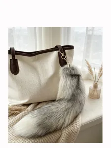 Gray-white faux fur tail charm with gold clasp hanging from a cream tote in a bright home setting