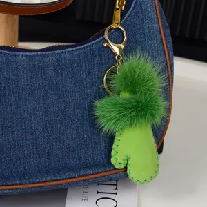Gros plan de pompons verts et d'un charm effet daim avec mousqueton doré sur un sac en jean