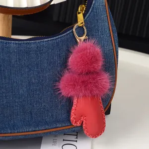 Gros plan sur un pompon rose en fausse fourrure et un charm en cuir rouge fixé au sac en denim bleu