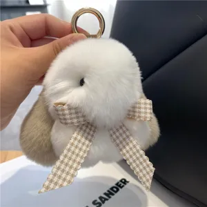 Nahaufnahme eines flauschigen Hasenanhängers in Weiß und Beige mit Karoschleife und Metallring