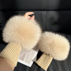 Beige fluffy fur wrist warmers with ribbed knit cuffs, shown worn against a dark leather sofa