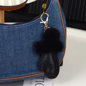 Gros plan : pompon noir et charm en cuir fixés à un sac en denim bleu avec mousqueton doré
