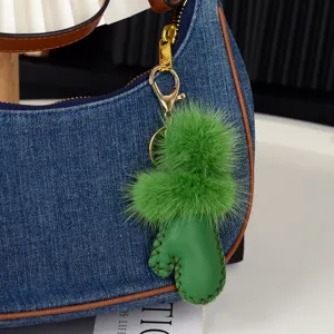 Pompon vert en peluche et cactus en cuir avec mousqueton doré, suspendus à un sac en denim
