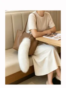 White fluffy tail charm with a gold clasp hanging from a brown handbag in a café setting