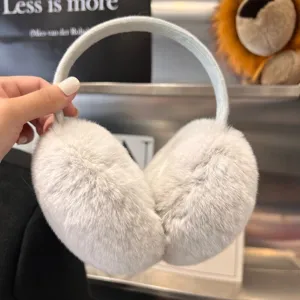 Light gray plush ear cups with a fabric-covered arch, held by hand against a blurred backdrop