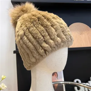 Side view of the camel-toned hat, showing its plush knitted texture and fluffy pom-pom