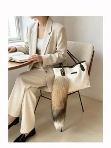 Seated woman with a book beside a cream tote with dark trim and a fluffy tail charm