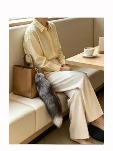 Gray and white fur tail charm with a gold clasp hanging from a brown tote bag in a café setting