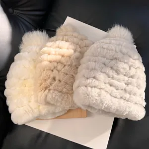 Three plush knit hats in cream, beige, and light gray with fluffy pom-pom tops, shown side by side
