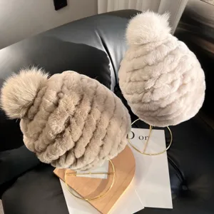 Two plush rib-knit hats in taupe and ivory, shown on stands with fluffy pom-pom details