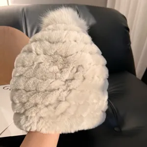 Close-up of a gray-white plush knitted hat with textured fur panels and a matching top pom-pom