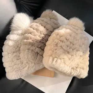 Two plush knit winter hats in cream and taupe, topped with fluffy pom-poms, shown side by side