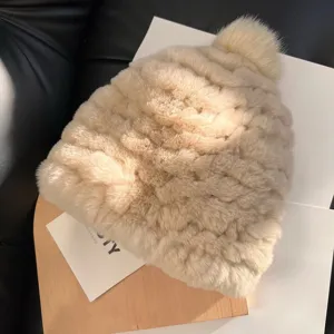 Close-up of a cream plush knit hat with textured stitches and a matching fluffy pom-pom