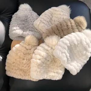Overhead view of plush ribbed knit hats in cream, gray and beige, some topped with fluffy pom-poms