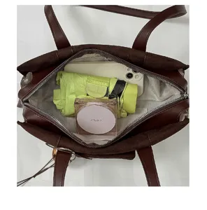 Top-down view into an open brown bag, showing its zip closure, gray lining, and stored essentials