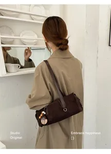 Lifestyle view of a brown suede-texture bag worn over the shoulder, with a charm and metal buckle