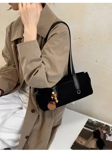 Black suede-textured bag worn over the shoulder, with a long strap and wooden bead charm
