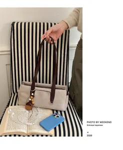 Hand-held taupe bag with dark brown handles and wooden bead charm on a striped chair
