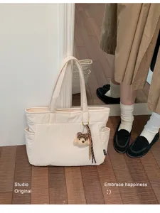 Sac cabas crème avec deux anses, poches latérales et porte-clés ourson, posé sur un sol en bois
