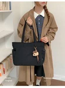 Modèle portant un sac noir à poches latérales avec un pendentif ourson en peluche en intérieur