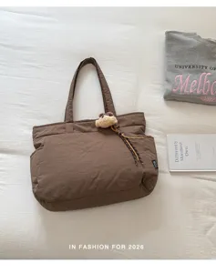 Vue à plat d’un sac brun avec breloque ourson et cordon tressé posé sur une literie blanche