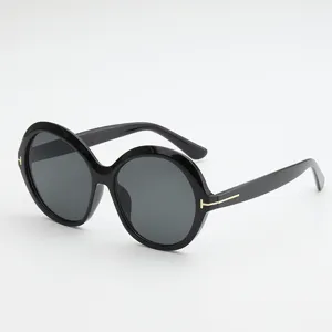 Black oversized round sunglasses with dark gray lenses and gold T-shaped temple accents, angled view