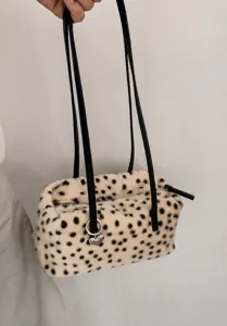 Detail einer cremefarbenen Plüschtasche mit schwarzen Punkten, langen Riemen und Herzanhänger