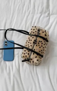 Draufsicht: cremefarbene Plüschtasche mit Punkten und schwarzem Riemen neben blauem Handy