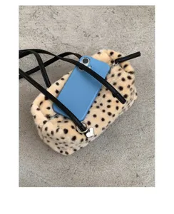 Gepunktete Plüschtasche mit schwarzen Riemen und silbernem Herzanhänger, ein Handy liegt darauf