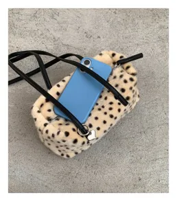 Beige Kunstpelztasche mit schwarzen Punkten, schwarzen Riemen und weißem Herzanhänger.