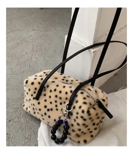 Detail einer gefleckten Kunstfelltasche mit schwarzen Lederriemen und silbernem Perlenanhänger