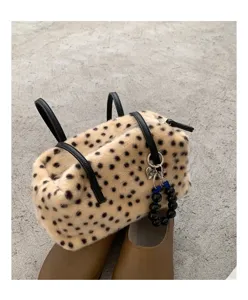 Detail einer gepunkteten Plüschtasche mit schwarzen Ledergriffen, Reißverschluss und Perlenanhänger