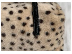Nahaufnahme von beigem Plüsch mit dunklem Tiermuster und kontrastierendem schwarzem Lederriemen