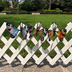 Three colorful butterfly ornaments with glass-like wings displayed along a white garden fence