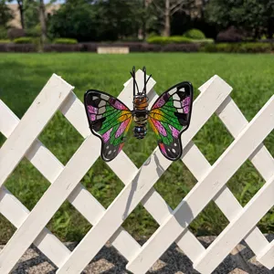 Colorful stained-glass butterfly ornament hanging on a white garden fence, with green lawn behind
