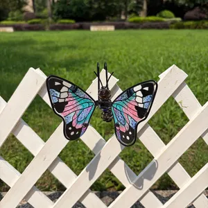 Colorful stained-glass butterfly with black metal edging displayed on a white garden fence