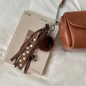 Detalle de un pompón marrón de pelo sintético con cintas, cuenta de madera y aro metálico