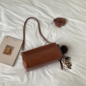 Vista cenital de un bolso marrón de polipiel, con correa desmontable y adornos de pompón