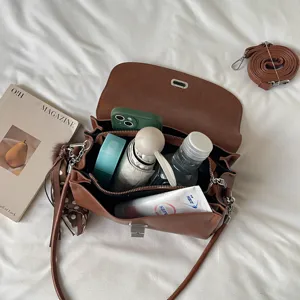 Vista superior de un bolso marrón abierto con teléfono y botellas sobre ropa de cama blanca