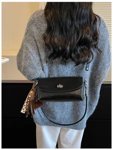 Vista trasera de un bolso negro con solapa, cierre plateado, pañuelo decorativo y correa larga