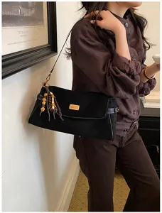 Sac noir porté à l’épaule, avec bordure en cuir, pompons en perles de bois et plaque métallique