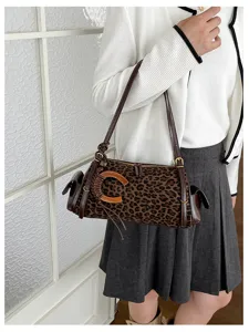 A model wears a brown leopard-print bag with dark straps, gold hardware, and a curved wooden accent.