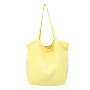 Vista frontal de un bolso amarillo con asas largas, pliegues suaves y letras blancas «beyou» y «merci»