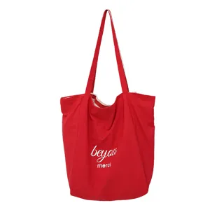 Vista frontal de un bolso tote rojo de nylon, con asas largas y las letras blancas «beyou» y «merci»