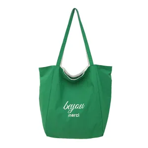 Vista frontal de una bolsa tote verde con letras blancas “beyou” y “merci” sobre fondo blanco.