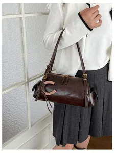 Brown glossy shoulder bag worn over a white knit top, with a C-shaped ornament and adjustable strap
